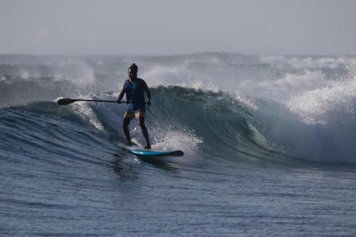 a man riding a wave on a surfboard in the ocean at Equator Village Maldives in Gan