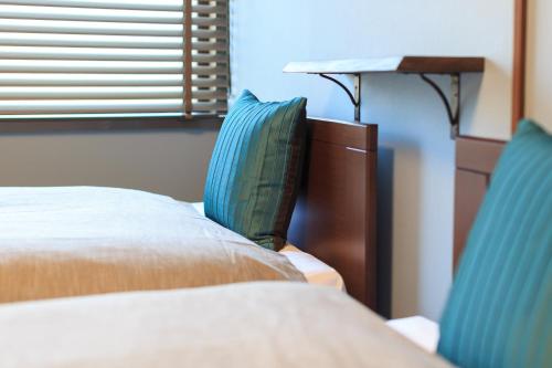 two beds with blue pillows in a room at Kulton Moct Kenroku in Kanazawa