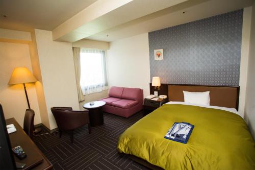 Habitación de hotel con cama y silla rosa en Hotel Green Hill Kagoshima, en Satsumasendai