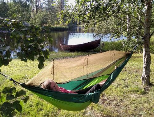 a woman laying in a hammock next to a lake at Hotelli Möhkön Rajakartano - Ilomantsi in Petkeljärvi