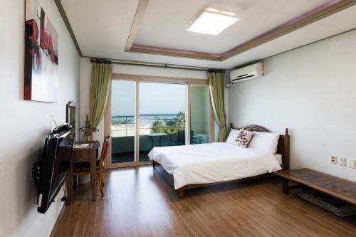 1 dormitorio con cama, escritorio y ventana en Jeju Bada Wi Olle Pension, en Seogwipo