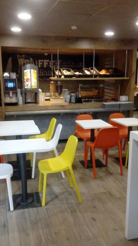 a restaurant with white tables and colorful chairs at ibis budget Dieppe Centre Port in Dieppe