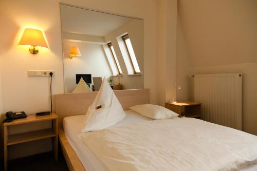 a bedroom with a white bed with a large mirror at Hotel Moerser Hof in Moers