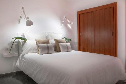 una camera da letto con un letto grande con lenzuola e cuscini bianchi di Maspalomas Suites a Maspalomas