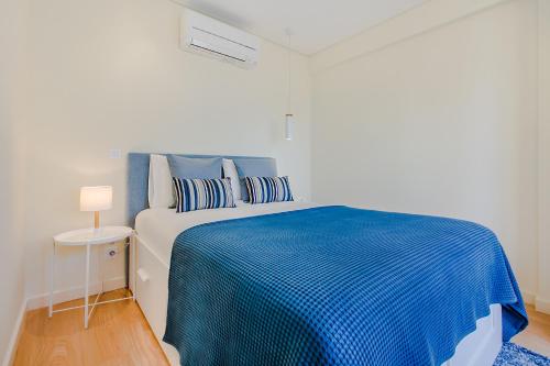 uma cama num quarto branco com um cobertor azul em Trindade Modern Flat no Porto