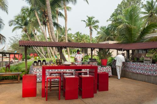 a restaurant with red tables and chairs and palm trees at Hotel Coucoue Lodge in Assinie
