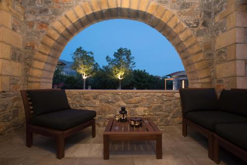 a patio with two chairs and a table in front of a stone wall at Calme Suites Mani in Agios Nikolaos