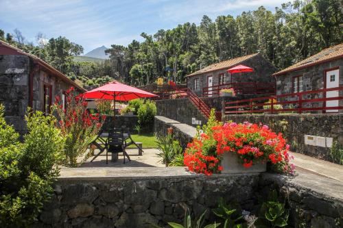eine Terrasse mit einem Tisch, roten Sonnenschirmen und Blumen in der Unterkunft Aldeia das Adegas in São Roque do Pico