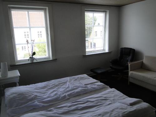 ein Schlafzimmer mit einem Bett und einem Stuhl sowie zwei Fenstern in der Unterkunft Thinghuskroen in Vestervig