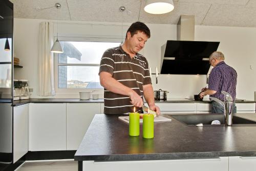 a man standing in a kitchen preparing food at Luksus-poolhus L21 in Harboør