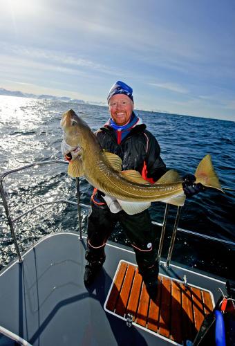 a man on a boat holding a large fish at Lyngen Experience Lodge in Nord-Lenangen