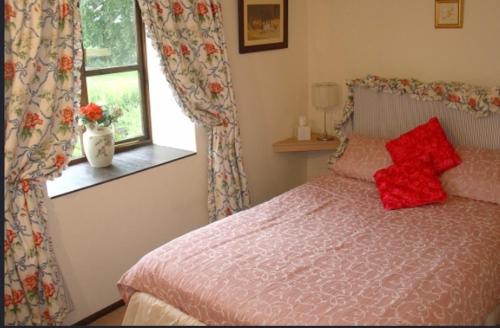 a bedroom with a bed with red pillows and a window at Forge Cottage in Merton