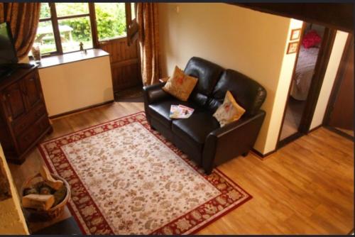 a living room with a black leather couch and a rug at Forge Cottage in Merton