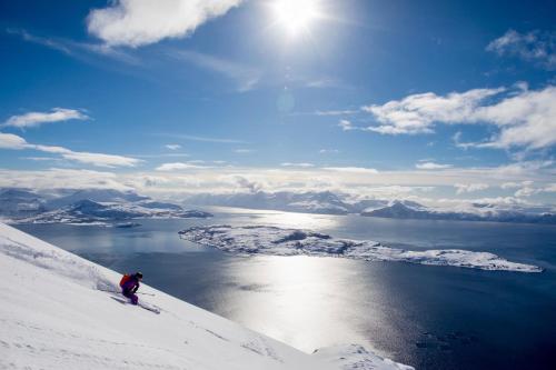 a person is skiing down a snow covered hill with a lake at Lyngen Experience Lodge in Nord-Lenangen