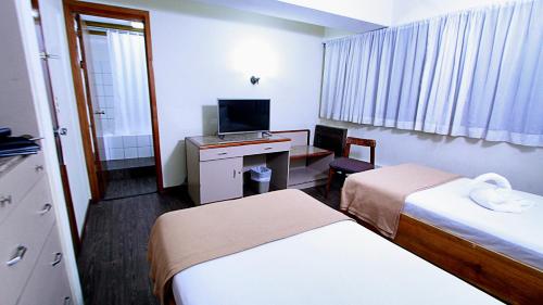 a hotel room with two beds and a desk with a television at Hotel Ambassador in San José
