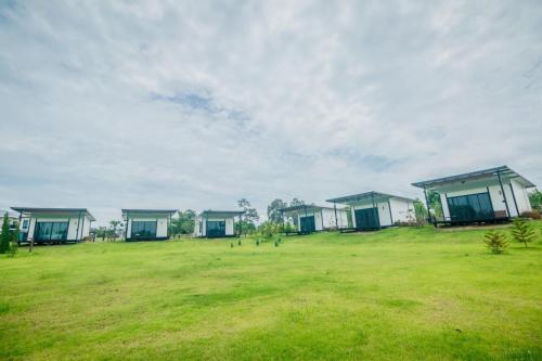 a row of houses in a grassy field with buildings at Mae On Village Resort in Roi Et
