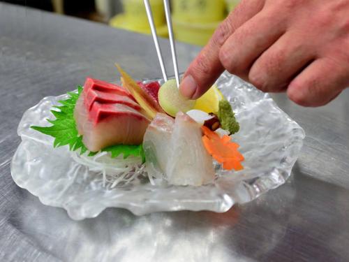 a person reaching for a piece of sushi on a glass plate at Bingoya in Kurashiki