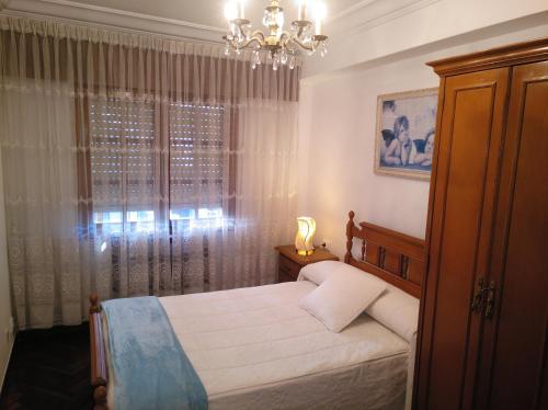 1 dormitorio con 1 cama con lámpara de araña y ventana en Apartamento Ciudad de la Cultura, en Santiago de Compostela