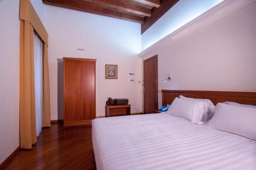 Schlafzimmer mit einem weißen Bett mit einem Kopfteil aus Holz in der Unterkunft Hotel Flora in Cagliari