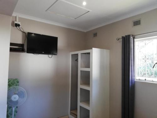 a room with a tv on the wall and a book shelf at Abendruhe Guest House in Eshowe