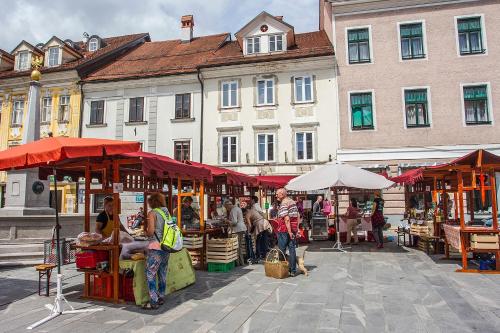 a group of people walking around a market with red umbrellas at Goldenfields apartment in Kranj