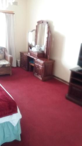 a bedroom with a dresser and a mirror and red carpet at Tshulu Tsha Nabe B&B in Bulawayo