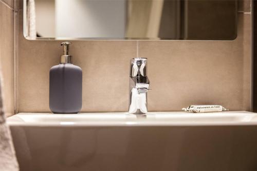 a bathroom sink with a bottle of soap and a mirror at TONI'S 2BD Apartment with Terrace next to Stadium in Athens