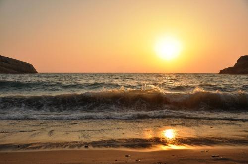 a beach with the sun setting over the ocean at Hotel Sofia in Matala