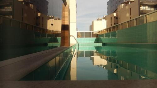 uma piscina com um reflexo de alguns edifícios em Praia do Morro - Guarapari - Apto 2 Quartos com Internet - Piscina - Ar Split - Edifício Gil Nogueira em Guarapari