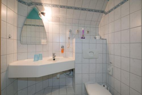 a white tiled bathroom with a sink and a toilet at Hotel Knöpel in Wismar