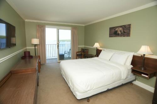 a bedroom with a large white bed and a balcony at Belknap Point Inn in Gilford