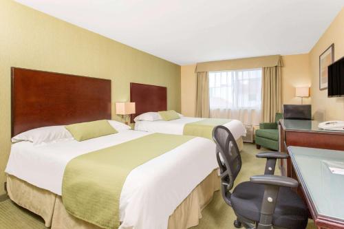 Habitación de hotel con 2 camas y escritorio en Ramada by Wyndham Williams Lake, en Williams Lake