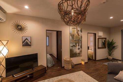 a living room with a television and a chandelier at BB Wakugawa Terrace in Nakijin