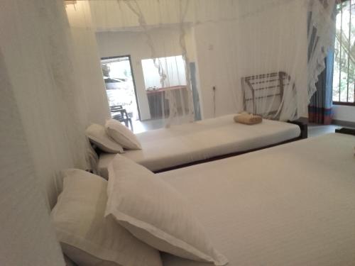 a bedroom with two beds with white sheets and pillows at Thusara Guesthouse in Mirissa