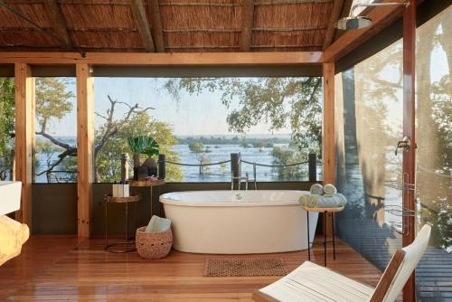 a bath tub in a room with a large window at Victoria Falls River Lodge in Victoria Falls