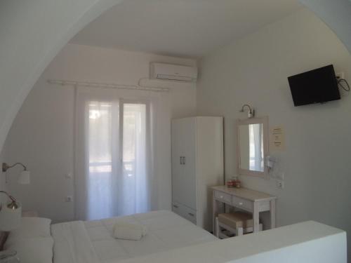 a white bedroom with a bed and a desk at Taxiarchis Studios in Áyios Yeóryios