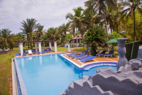 a swimming pool with blue chairs and palm trees at African Queen Lodge in Assinie
