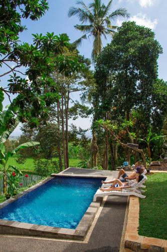 a swimming pool with two people sitting on lounge chairs in a resort at Mandhasativa Homestay in Singaraja