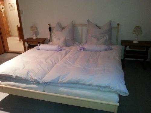 a large white bed with white sheets and pillows at Ferienhaus Kraihof, Münchner Straße 234 in Gmund am Tegernsee