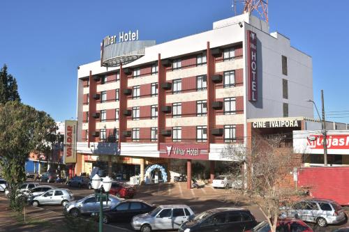 a large building with cars parked in a parking lot at Hotel Vilhar in Ivaiporã