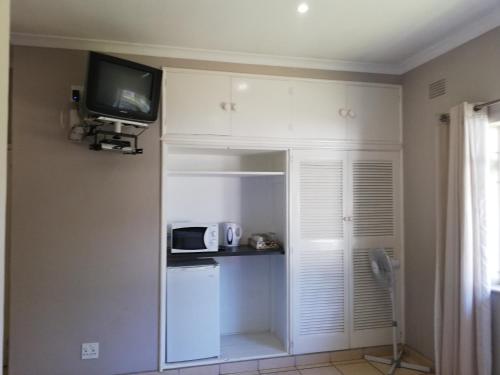 a kitchen with white cabinets and a tv on the wall at Abendruhe Guest House in Eshowe