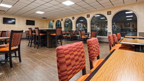 a restaurant with wooden tables and chairs and windows at Best Western Tulsa Airport in Tulsa