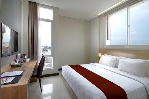 a hotel room with a bed and a desk and window at D'Kalpa Hotel Demangan Yogyakarta in Yogyakarta
