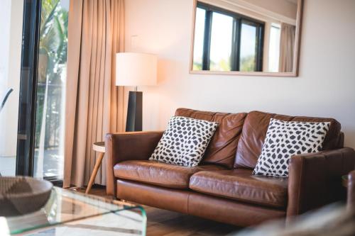 a living room with a brown leather couch with two pillows at The Point Coolum in Coolum Beach