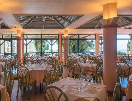 a dining room with tables and chairs and windows at Dom Pedro Garajau in Caniço