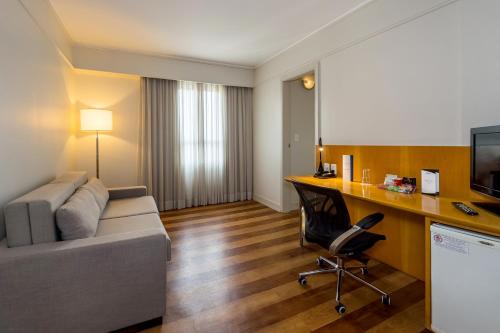 a living room with a couch and a desk with a computer at Pergamon SP Frei Caneca by Accor in Sao Paulo