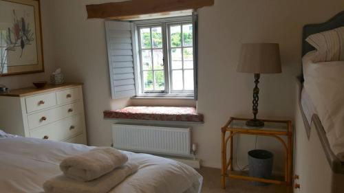 a bedroom with a bed and a window with a bench at Pilchards Cottage in Noss Mayo