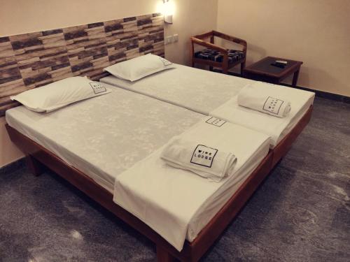 a bedroom with two beds with white sheets and a chair at Hotel Wins in Kanyakumari