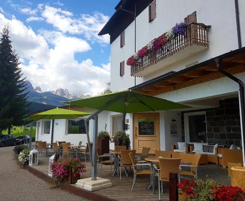 a restaurant with tables and chairs and green umbrellas at Ciasa Alpina Relax Hotel in Moena