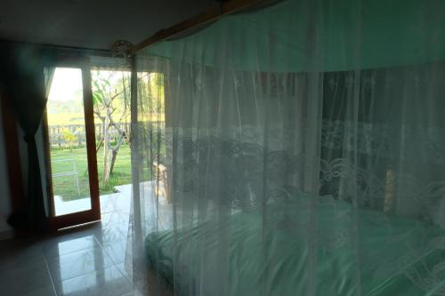 a bedroom with a bed with a curtain and a window at THE NYAMO surf & stay in Pulukan